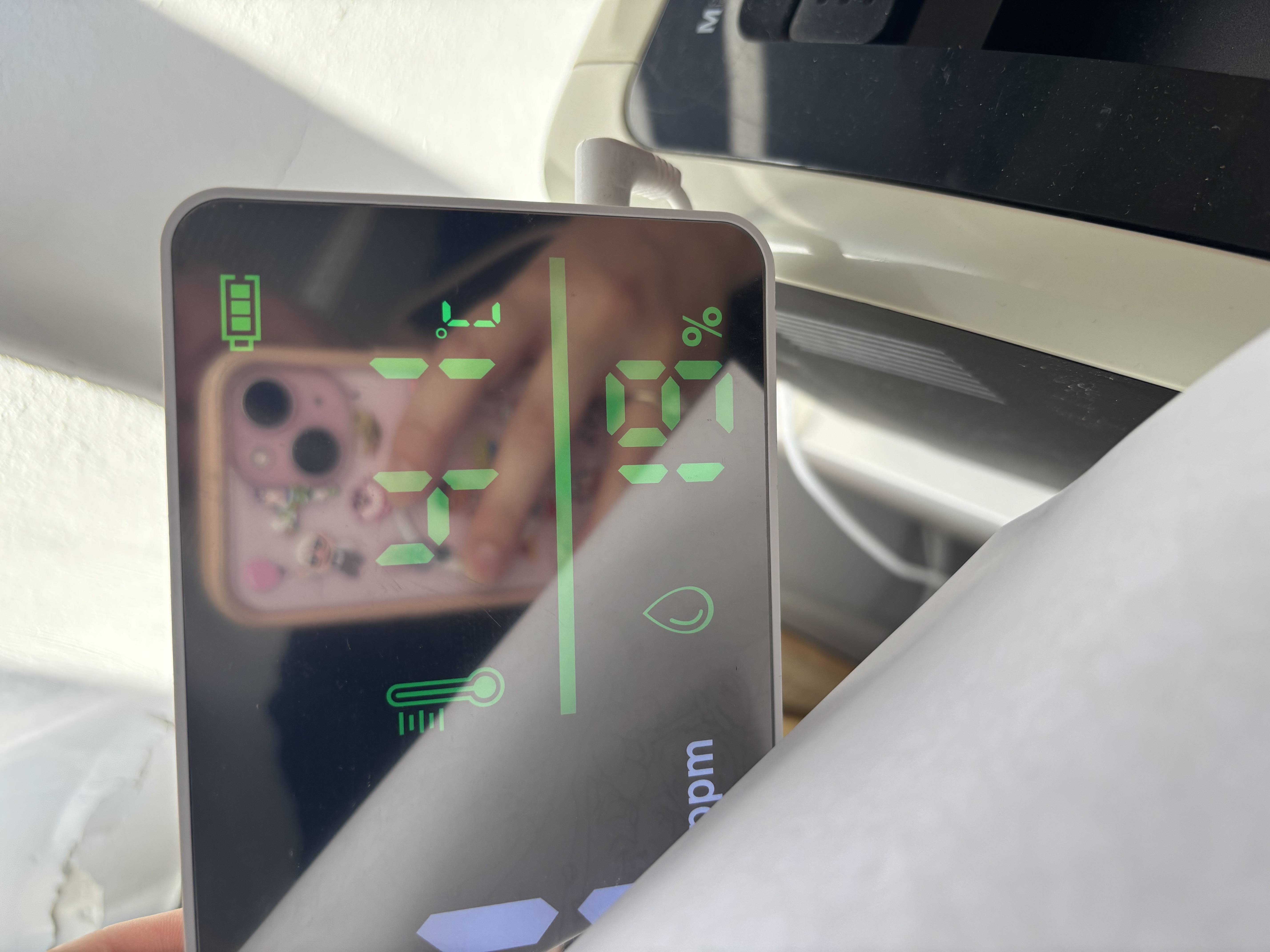 Person holding a black device with green numbers and symbols, including a thermometer and oxygen level indicator, in a classroom. Indicating 41°C. 