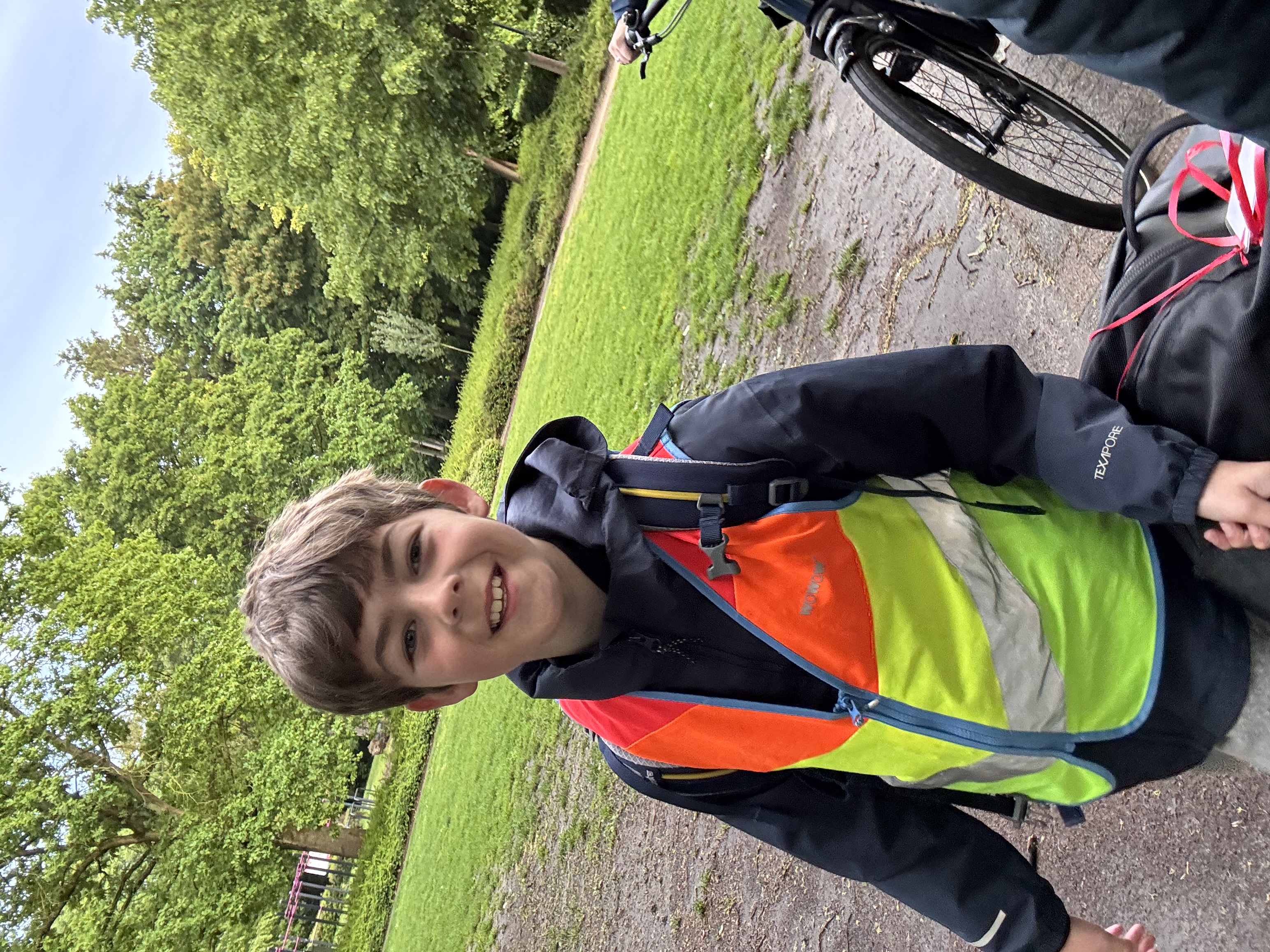 Een jongen in een fluovest die door een park wandelt met zijn koffer.